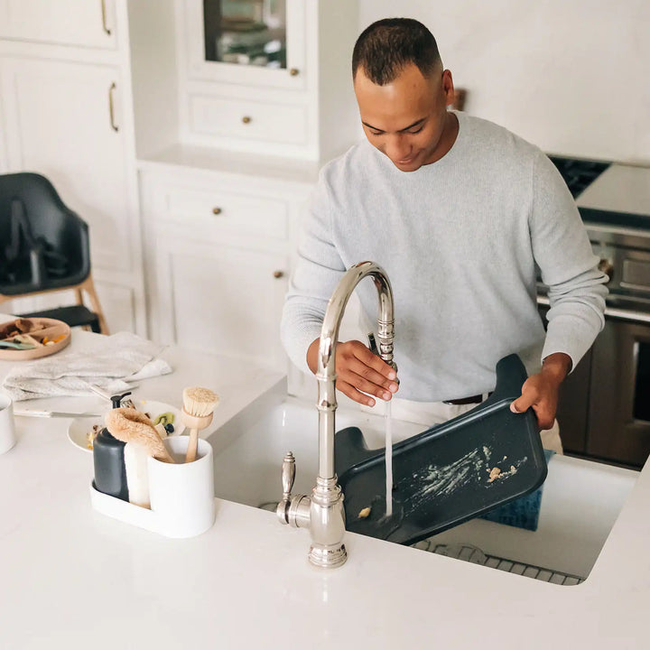 Man washing dishes in a kitchen with a modern faucet.
