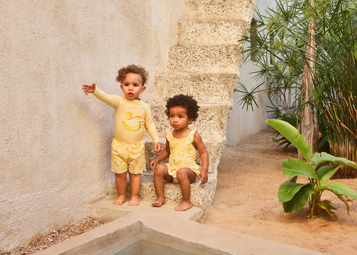 Two kids, one wearing Nalani Lemon Banana Swimsuit by Molo