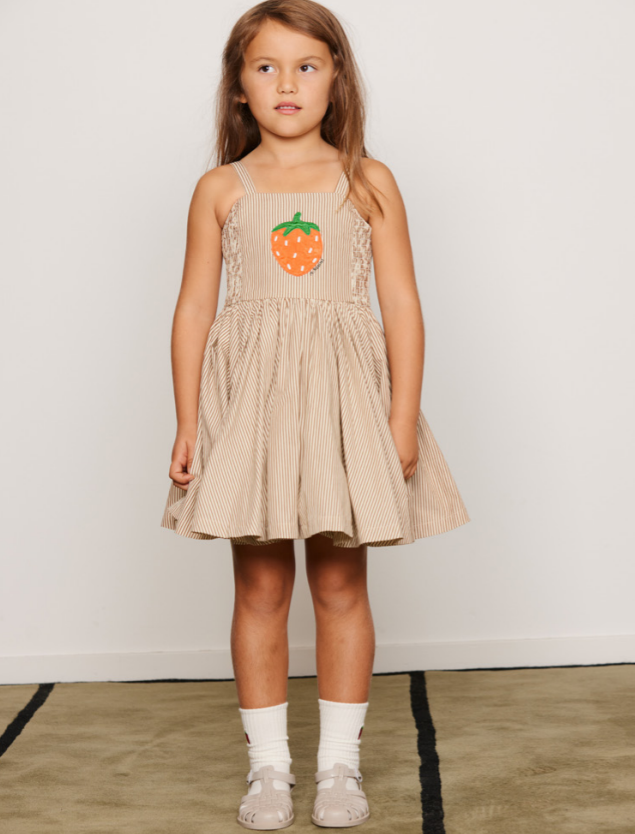 Young girl wearing a beige dress with a strawberry design on a plain background Poplin Strawberry Patch Smock Dress by Mini Rodini