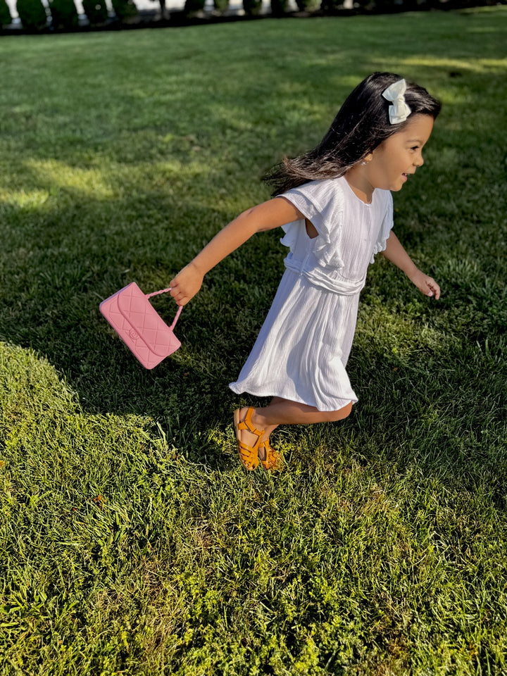 Young girl in a white dress running on grass with a pink Chanelini snack tote handbag