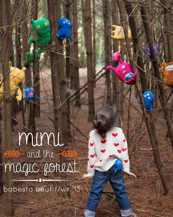 Child in a forest with colorful plush toys attached to trees, featuring 'mimi and the magic forest' text.