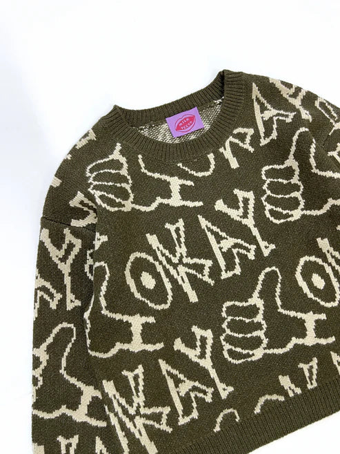 Children’s oversized crewneck sweater in pink with hand-drawn ‘okay’ lettering and thumbs-up doodle, laid flat to show boxy fit and ribbed trim