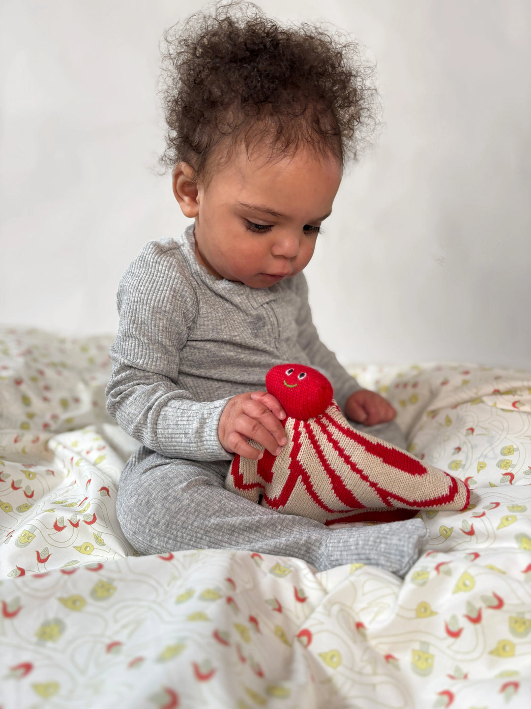 Baby playing with a Red and white flower-shaped lovey by Javiera Varas  on a patterned blanket