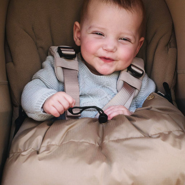 Baby sitting in a beige footmuff  by Bugaboo