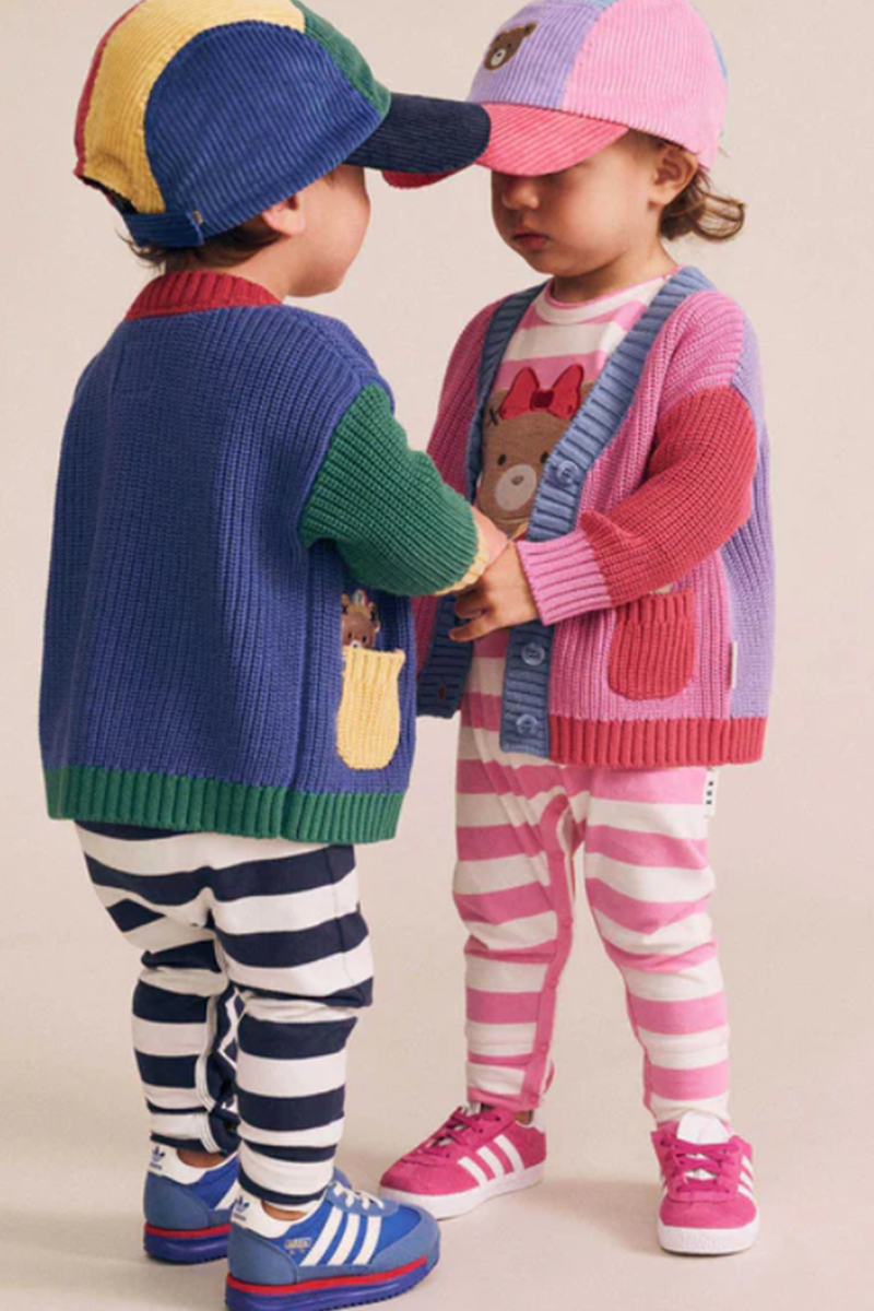 Two children wearing colorful clothing and hats, standing close to each other on a plain background.