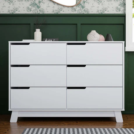 White dresser with multiple drawers against a green wall.