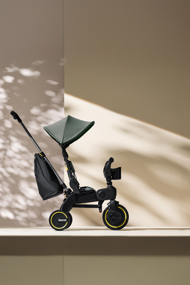 Black children's scooter with green seat on a light surface with shadows