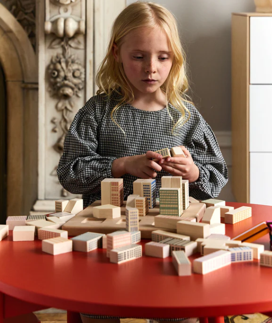 Child playing with wooden building blocks on a red table
